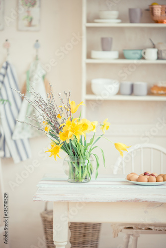 Bouquet of yellow flowers of daffodils in a glass vase on a wooden table in a bright room