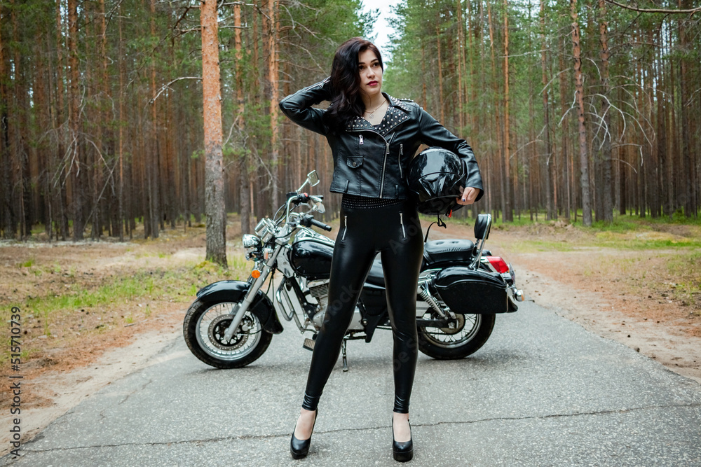 Fototapeta premium A girl in tight black leather stands next to a motorcycle.