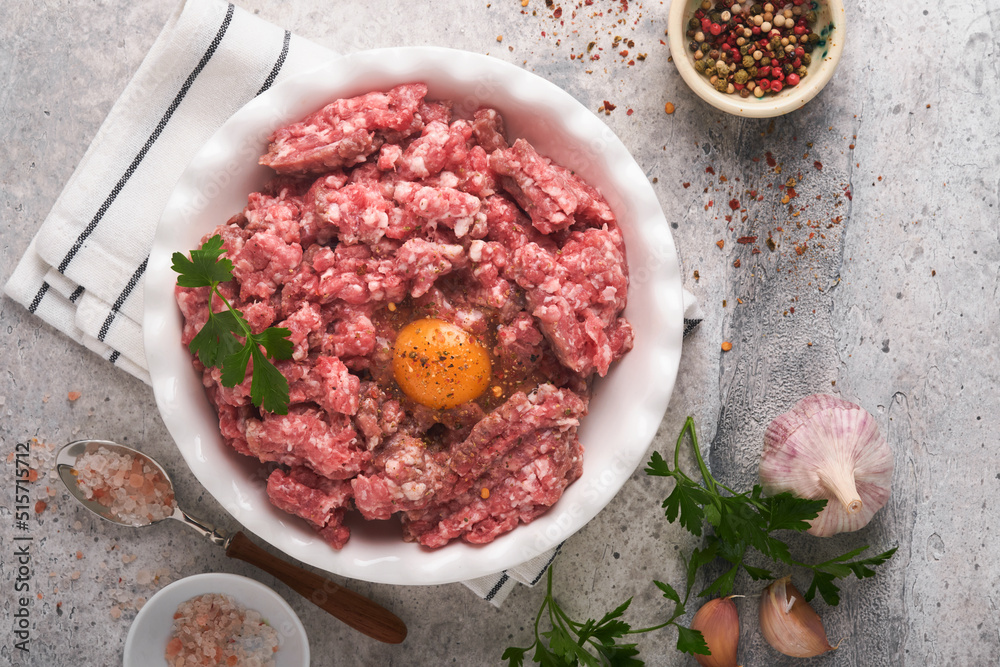 Raw minced meat. Ground meat beef, pork or lamb spices, herbs and eggs on white plate on light grey concrete background. Fresh minced meat ready for cooking. Food cooking background. Top view. Raw minced meat. Ground meat beef, pork or lamb spices, herbs and eggs on white plate on light grey concrete background. Fresh minced meat ready for cooking. Food cooking background. Top view.