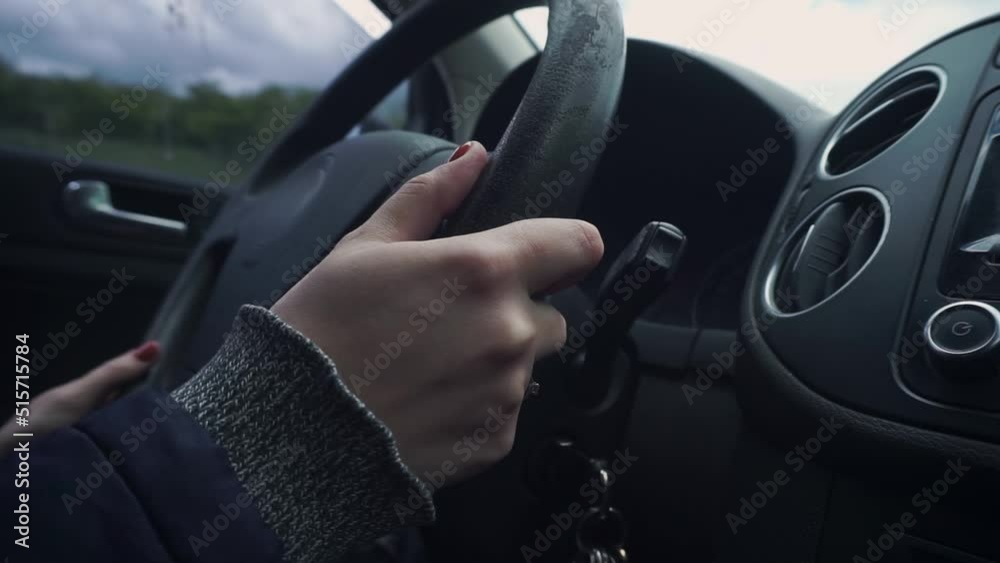 Woman's hands are turning the old steering wheel. Red manicure. Ring on the finger. Sleeves, jacket, jacket, car interior, salon. Passes under the bridge. Handheld shooting. Day, overcast Woman's hands are turning the old steering wheel. Red manicure. Ring on the finger. Sleeves, jacket, jacket, car interior, salon. Passes under the bridge. Handheld shooting. Day, overcast