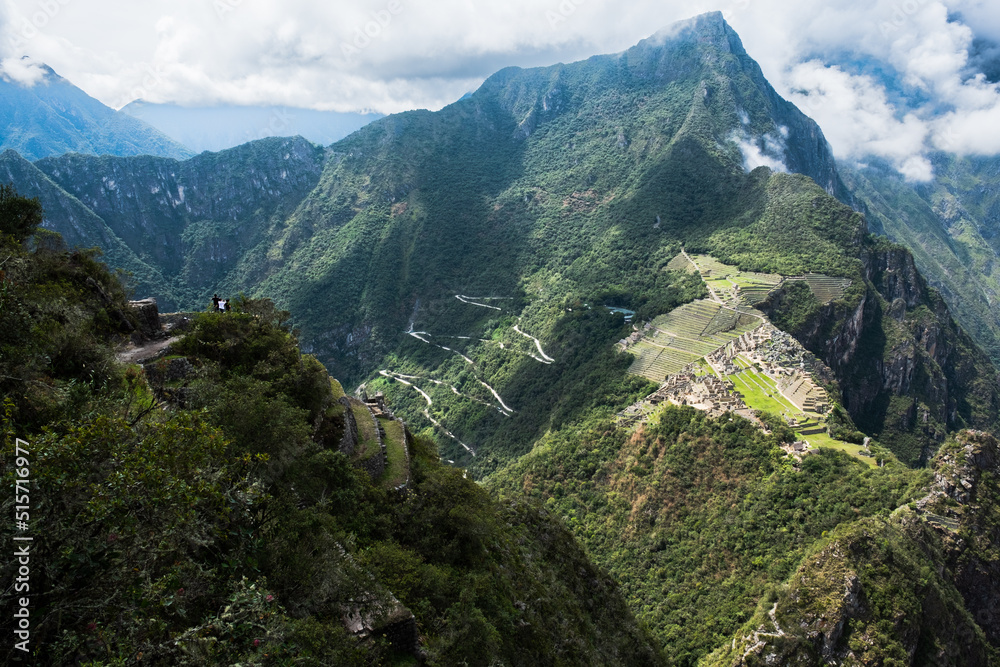 the winding road leading to Machu Picchu as seen from the summit of Huaynapicchu with small tourists in the foreground