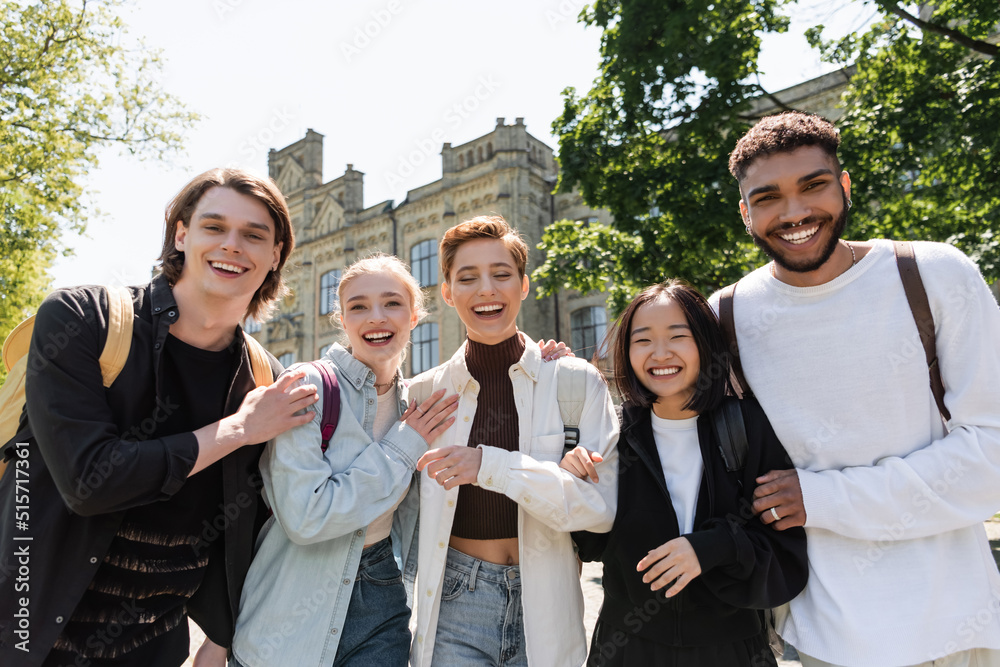Obraz premium Positive multiethnic students hugging and looking at camera outdoors.