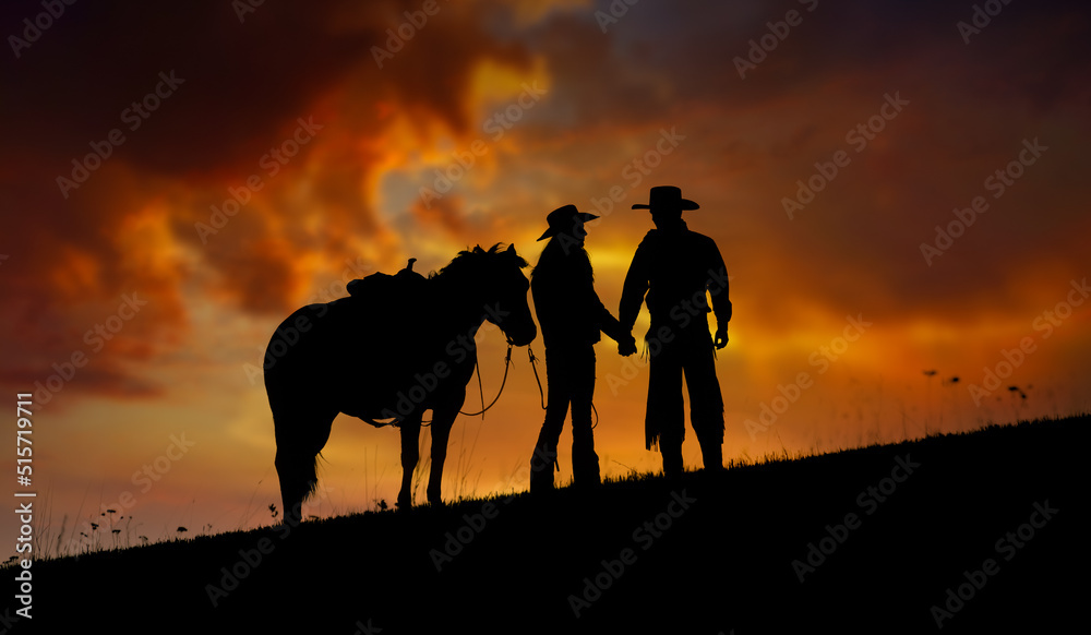 A cowboy couple hold hands against a sunset sky