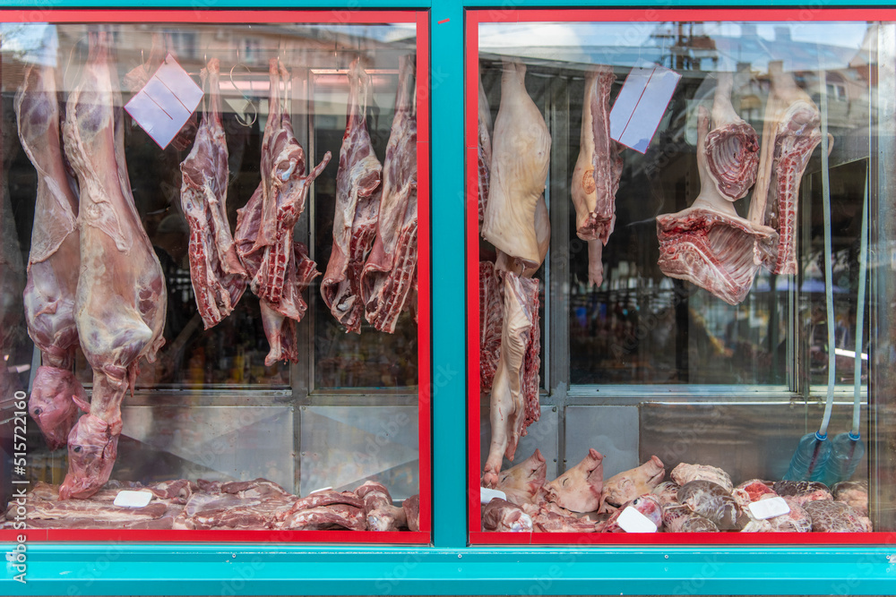 Fresh hanging meat carcass on a stylish butcher shop window and its fridged counter with meat. 