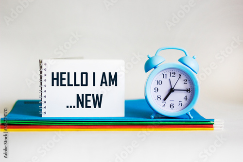 HELLO I AM NEW text on notepad with assorted folders and clock on white background photo