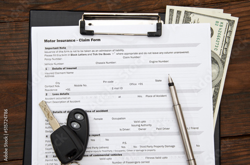 Motor insurance claim form, car key and pen on wooden desc