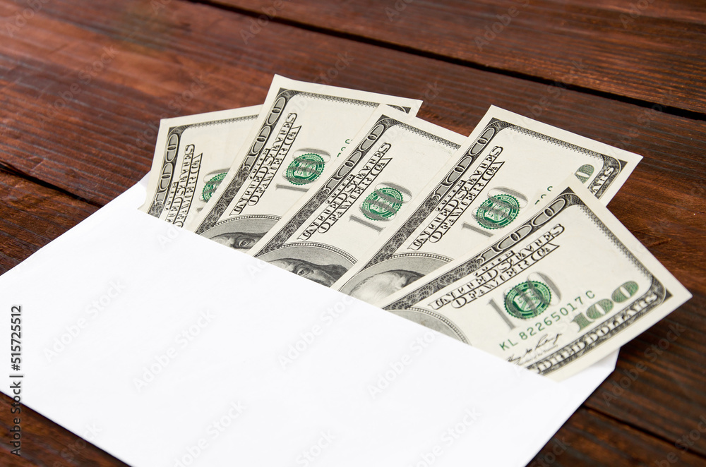 Banknotes of 100 dollars in an white envelope on a wooden desc Banknotes of 100 dollars in an white envelope on a wooden desc