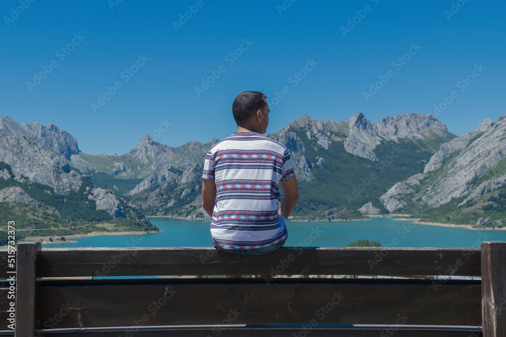 Fototapeta premium Chico joven observando las montañas de Riaño en desde un banco