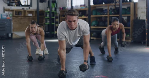 Active people using dumbbells for plank and renegade rows while training in a gym. Group of focused and diverse athletes exercising with heavy weights to gain muscle and endurance in a fitness class photo