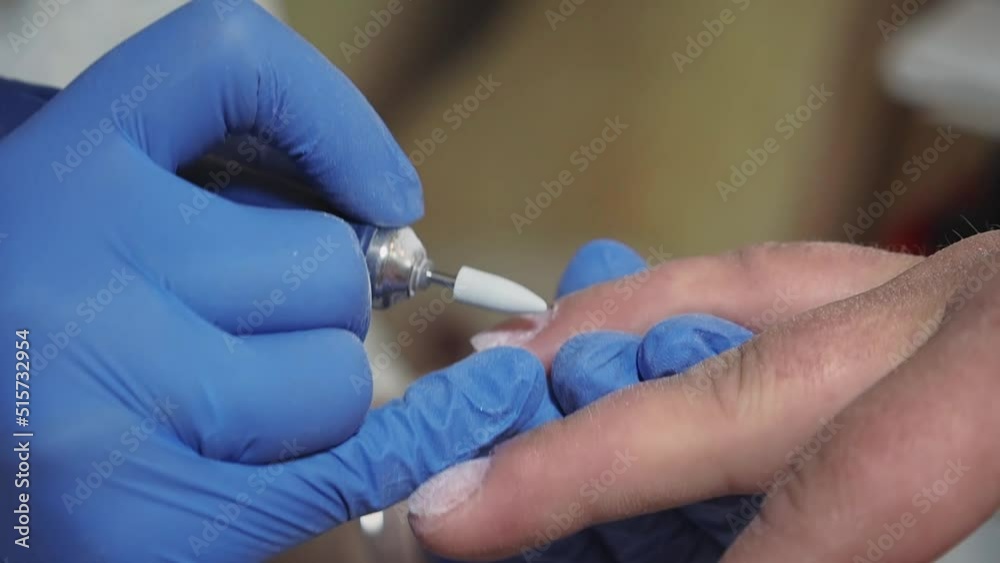 Manicurist master removing cuticles. Processing of rough cuticles and lateral folds of male nails on hands with a conical instrument. Medical hardware manicure in a beauty salon