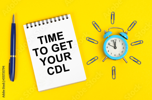 On a yellow surface there is an alarm clock, a pen and a notepad with the inscription - Time to Get Your CDL photo