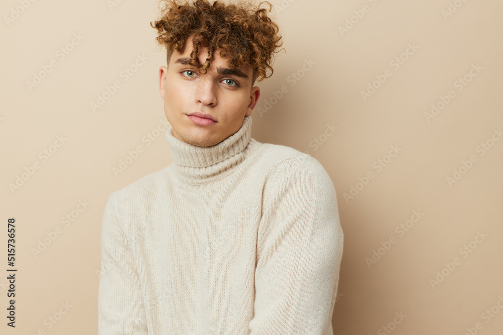 Fototapeta premium a close horizontal portrait of a handsome, handsome man standing on a beige background in a light turtleneck, looking pleasantly into the camera