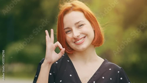 Female outdoors portrait happy caucasian woman model feminine lady shows okay hand gesture everything fine perfect sign smiling pretty girl successful student stand outside satisfied with good service photo