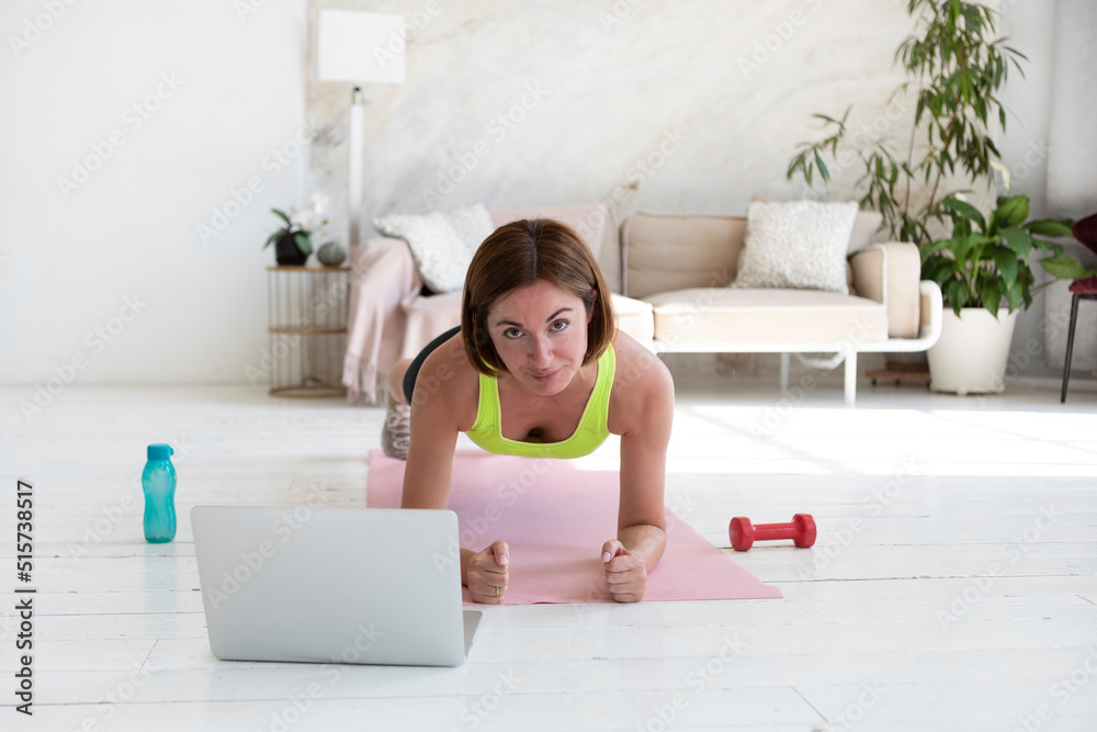 Attractive sporty woman doing plank exercise online at living room. Healthy lifestyle and home training concept Attractive sporty woman doing plank exercise online at living room. Healthy lifestyle and home training concept