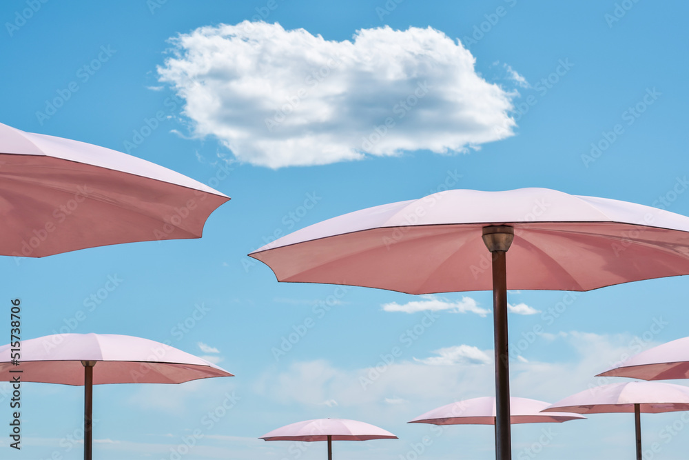 Pink beach umbrellas against blue sky with white cloud