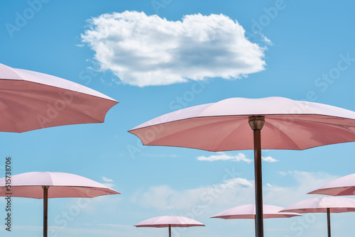 Pink beach umbrellas against blue sky with white cloud