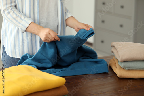 Woman folding clothes at wooden table indoors, closeup
