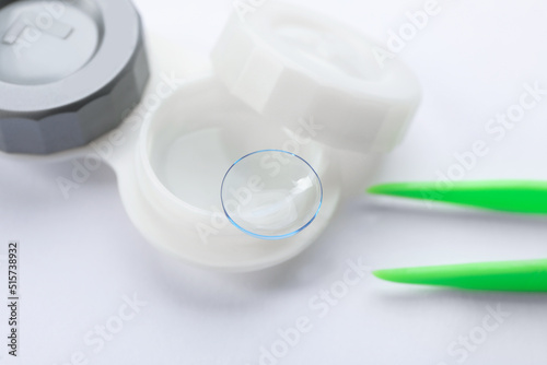 Case with contact lens and tweezers on white background, closeup