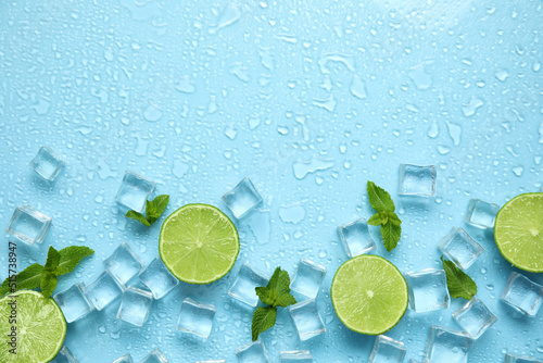 Ice cubes, mint and cut limes on turquoise background, flat lay with space for text. Refreshing drink ingredients