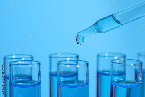 Dripping reagent into test tube on light blue background, closeup and space for text. Laboratory analysis