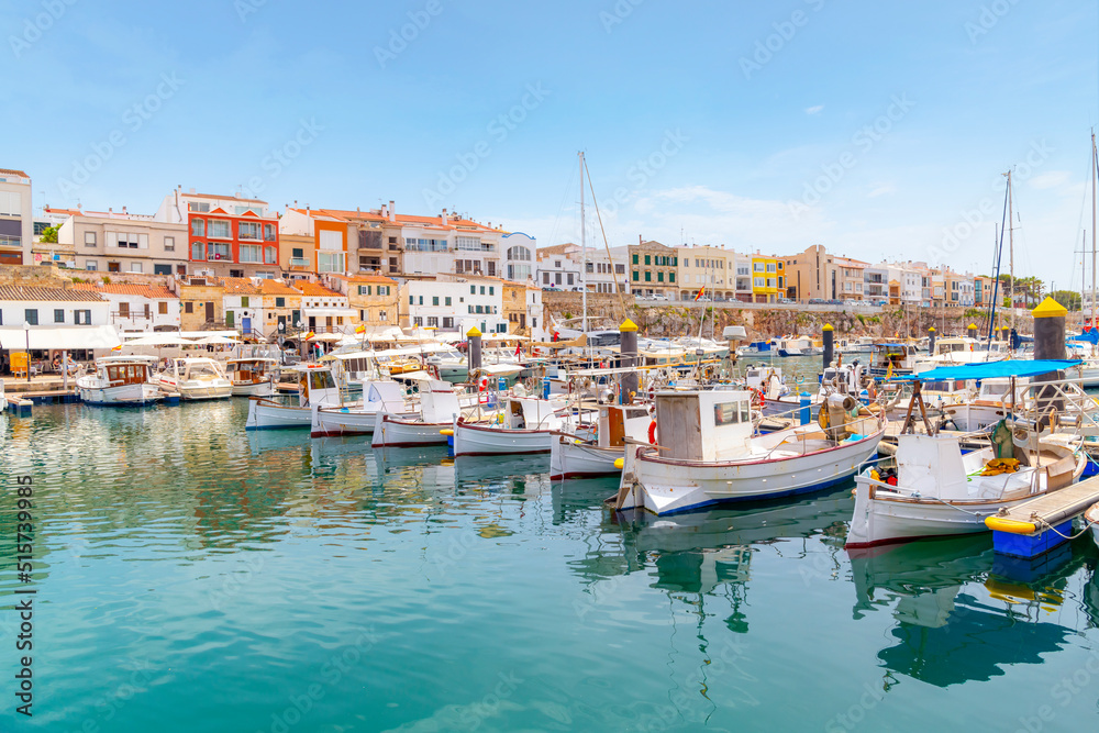 Boats line the picturesque marina port harbor at Ciutadella de Menorca, Spain, a small Balearic island in the Mediterranean Sea, with the colorful village in view.