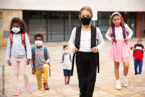 Portrait of tween schoolgirl in protective face mask with rucksack on her way to college on warm fall day. Back to school after lockdown concept.