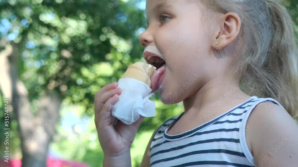 Smiling little girl eats ice cream. Close-up portrait of blonde girl sitting on park bench and eating ice cream and smiles. Slow motion, Camera moves around Smiling little girl eats ice cream. Close-up portrait of blonde girl sitting on park bench and eating ice cream and smiles. Slow motion, Camera moves around