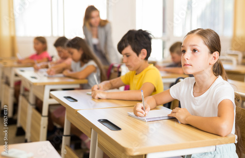 Portrait of cute intelligent schoolgirl who writing exercises at lesson in primary school