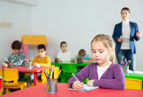 Portrait of cute diligent schoolgirl writing exercises at lessons in primary school