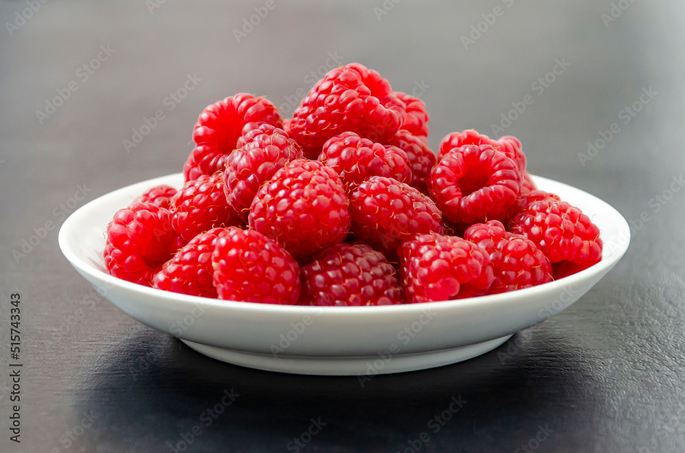 Raspberries on a white plate. Dark background. Close up Raspberries on a white plate. Dark background. Close up