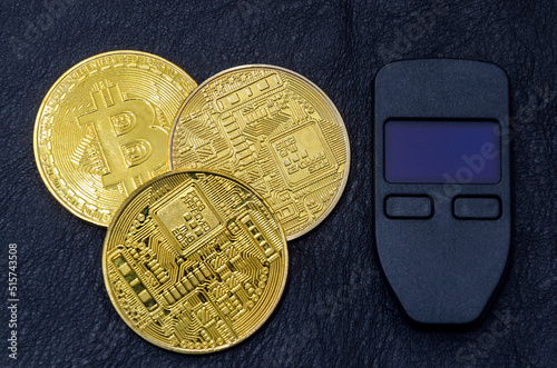 Gold bitcoins (physical symbol of bitcoins) with a hardware crypto wallet on a dark black leather background. The concept of saving cryptocurrencies. photo