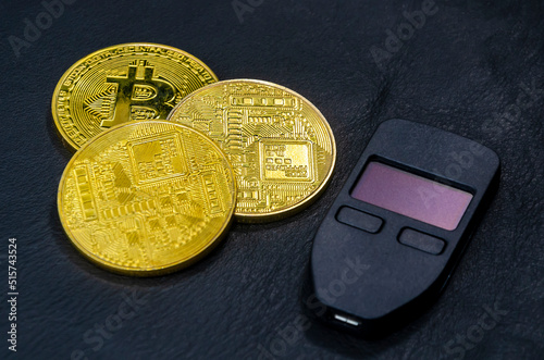 Gold bitcoins (physical symbol of bitcoins) with a hardware crypto wallet on a dark black leather background. The concept of saving cryptocurrencies. photo