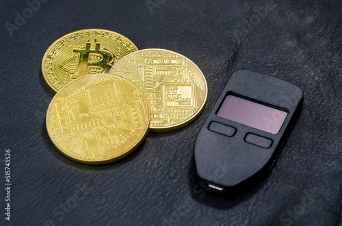 Gold bitcoins (physical symbol of bitcoins) with a hardware crypto wallet on a dark black leather background. The concept of saving cryptocurrencies. photo