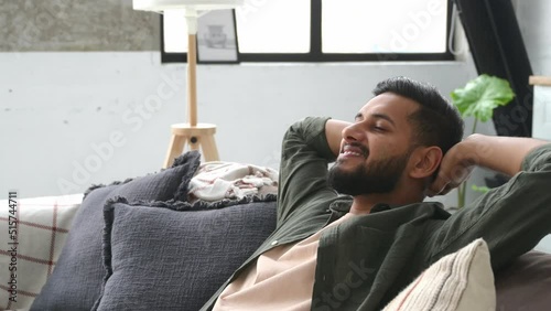 Satisfied calm arabian or indian attractive young man relaxing on the sofa at home in the living room, resting after a hard day's work, closed his eyes, put his hands behind his head, smiles happily