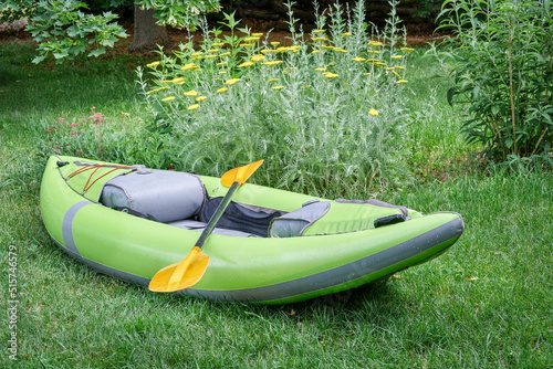 green inflatable whitewater one person kayak with a paddle in a backyard ready for a paddling adventure