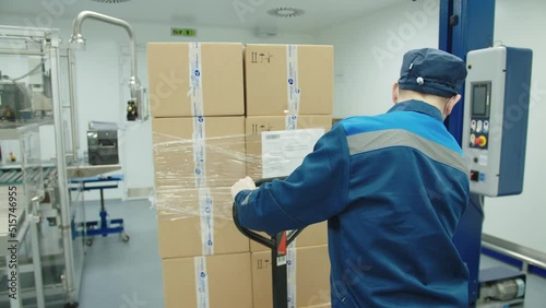 Back view of loader operating manually the fork truck at the pharmaceutical plant. factory worker in protective mask and uniform transports the batch of packaged boxes of medicine.