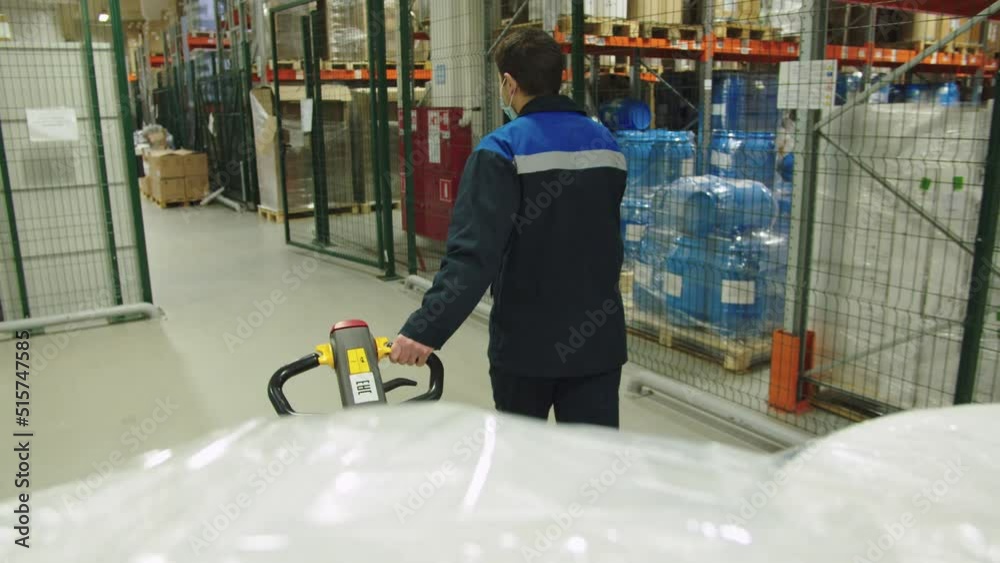Back view of forklift operator in special uniform pulling the batch of packaged containers of medicine. loader transports cargo trolley at the producing warehouse. Back view of forklift operator in special uniform pulling the batch of packaged containers of medicine. loader transports cargo trolley at the producing warehouse.