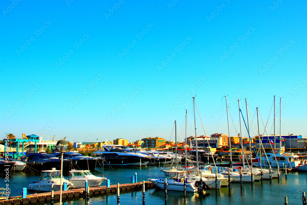 Peaceful scenery of the Fano port with multiple huge and small boats docked to it and the serene waters of the Adriatic Sea washing them on a pleasant summer day