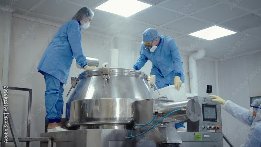 Pharmaceutical workers in protective masks and uniform work with medical equipment at medicine manufacturing factory. people pour the substance to automated machine for mixing and making drugs.