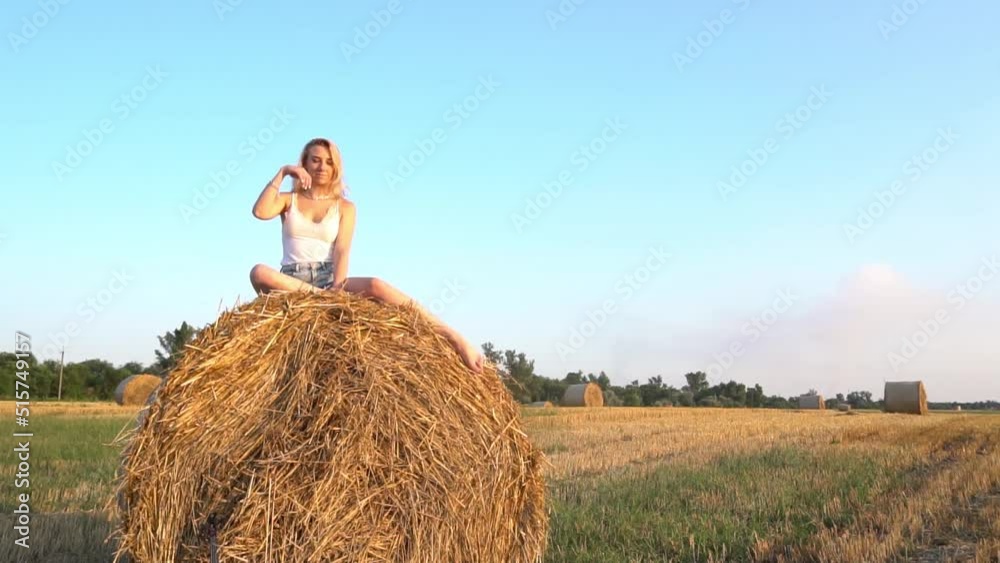Beautiful sexy girl sitting on haystack roll on harvested wheat field Beautiful sexy girl sitting on haystack roll on harvested wheat field