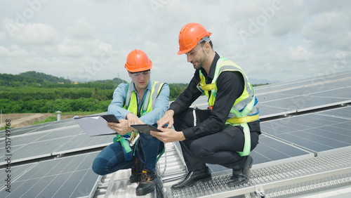 Engineer and construction worker examining solar panels on rooftop. © 2B