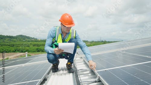 A young engineer inspects the solar panels on the factory while looking at the camera.