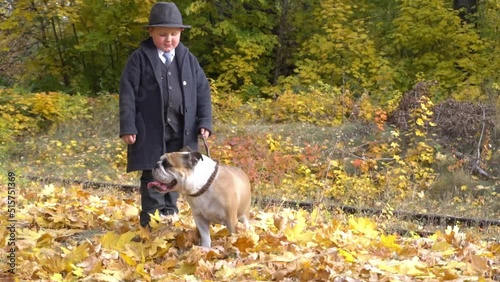 Cute little boy in black suit with his pet bulldog in autumn park