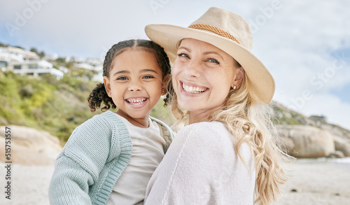 Portrait of a mature mother and her biracial innocent little daughter smiling and standing on the beach smiling. A happy woman and her adopted girl bonding on a day out during a summer vacation photo