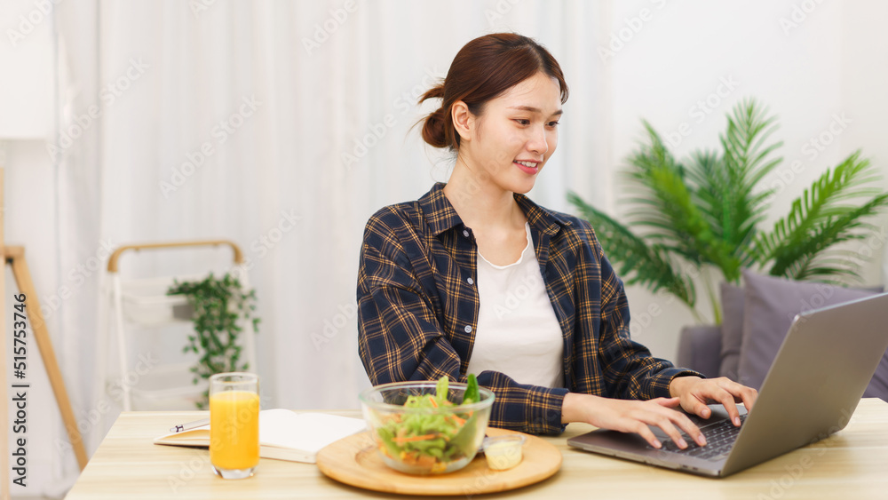 Lifestyle in living room concept, Young Asian woman eating vegetable salad and working on laptop Lifestyle in living room concept, Young Asian woman eating vegetable salad and working on laptop