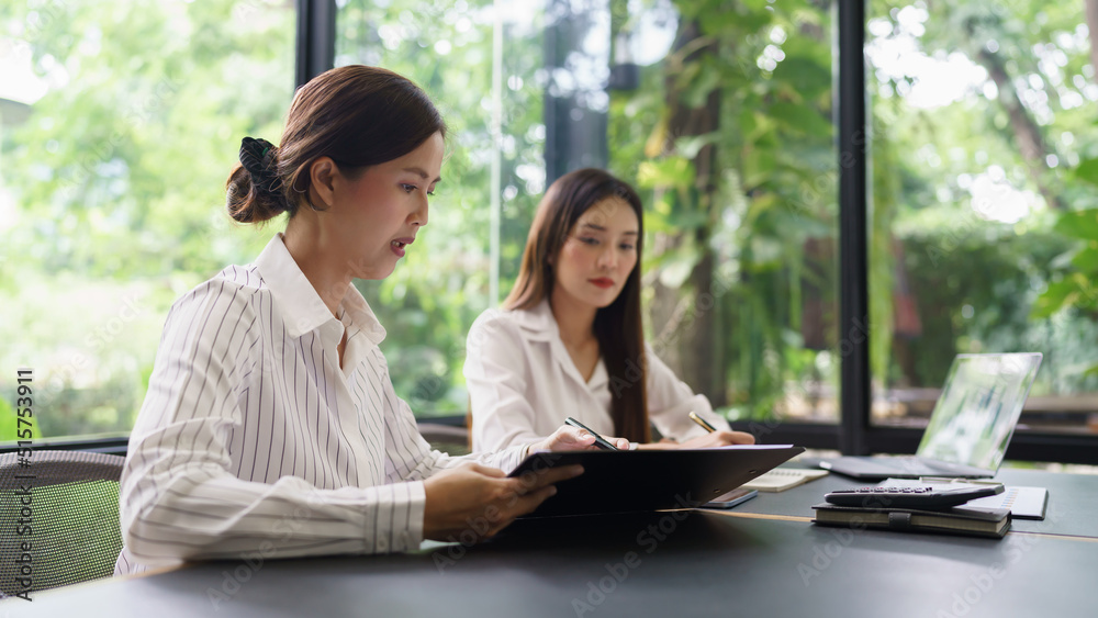 Coworker business concept, Two businesswoman discussing financial report and take notes on notebook Coworker business concept, Two businesswoman discussing financial report and take notes on notebook