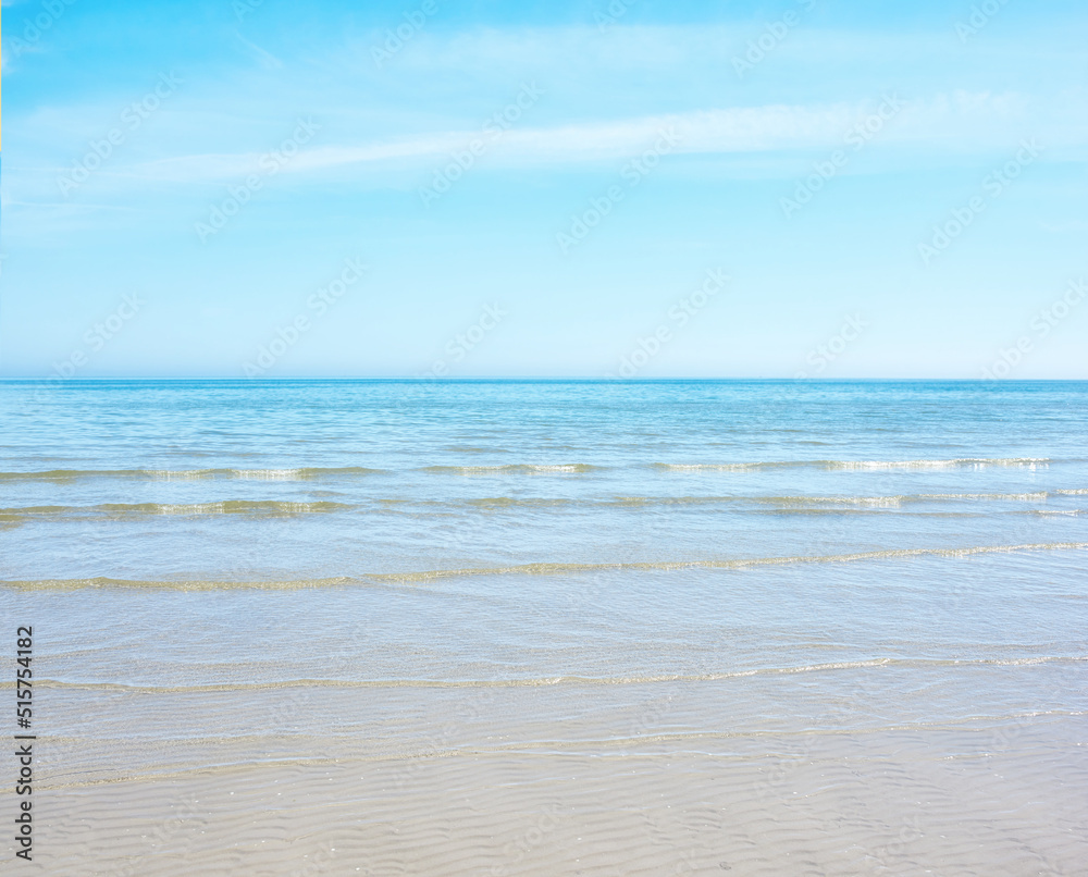 Copy space at the beach with a blue sky background above the horizon. Calm ocean waves across an empty sea along the sandy shore. Peaceful and tranquil landscape for a relaxing and zen summer holiday