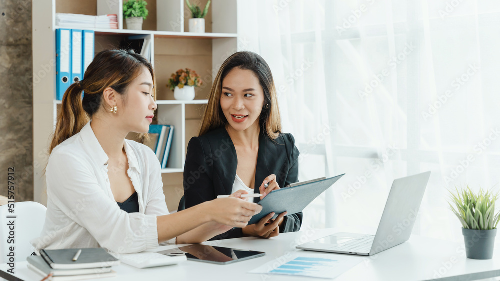 Two Asian female office workers working together with laptop at the white working desk in the comfortable meeting room. Two Asian female office workers working together with laptop at the white working desk in the comfortable meeting room.