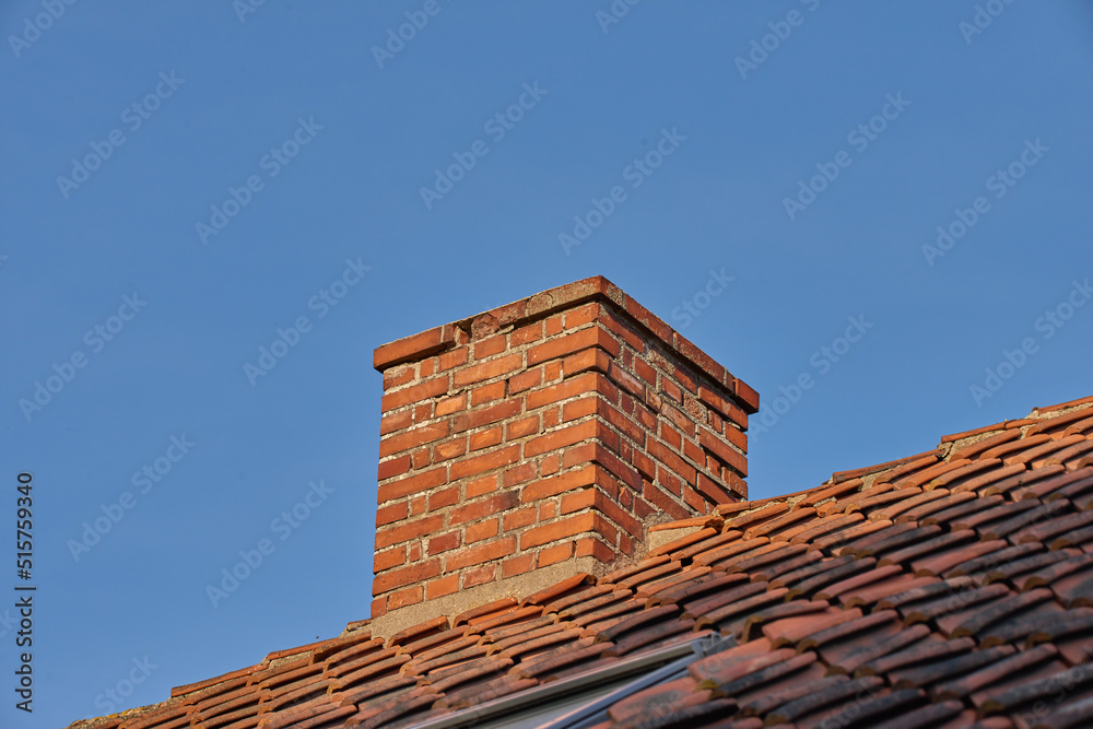 Copy space with a chimney on the rooftop of a house or building against a blue sky background. Brick construction of an exterior escape chute for ventilation of air and smoke from a fireplace or oven Copy space with a chimney on the rooftop of a house or building against a blue sky background. Brick construction of an exterior escape chute for ventilation of air and smoke from a fireplace or oven