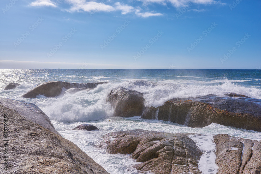 A rocky shore and a view of the ocean with waves, blue sky copy space, and a horizon in the background in Camps Bay, Cape Town, South Africa. Calm, serene, tranquil beach and nature scenery A rocky shore and a view of the ocean with waves, blue sky copy space, and a horizon in the background in Camps Bay, Cape Town, South Africa. Calm, serene, tranquil beach and nature scenery